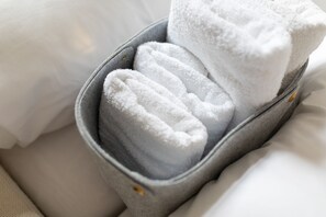 A gray fabric container with a white towel inside, placed on a bed with white bedding.