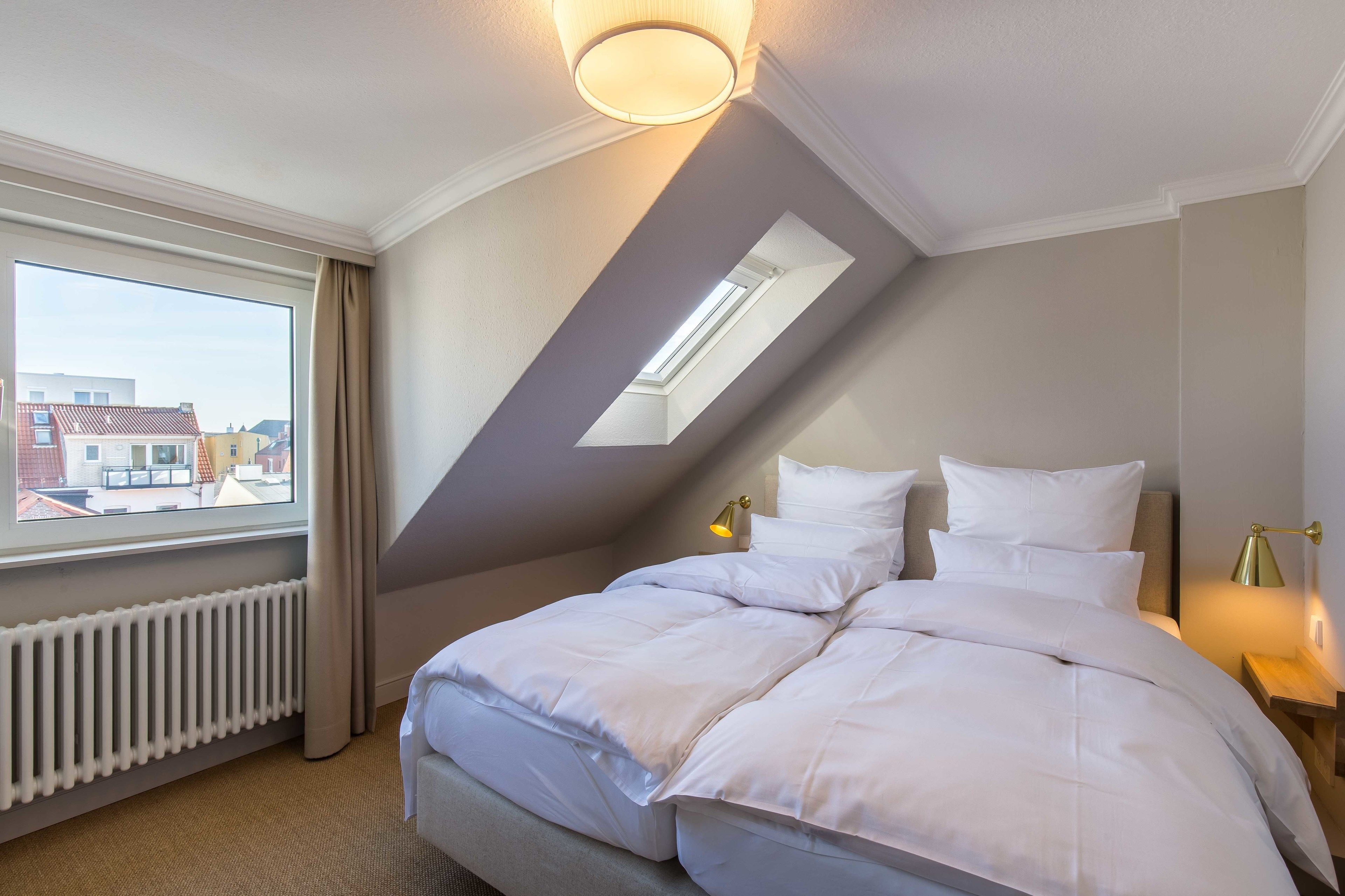 Ein Hotelzimmer mit einem großen Bett, einem Oberlicht, einer Heizung und Blick auf Gebäude.