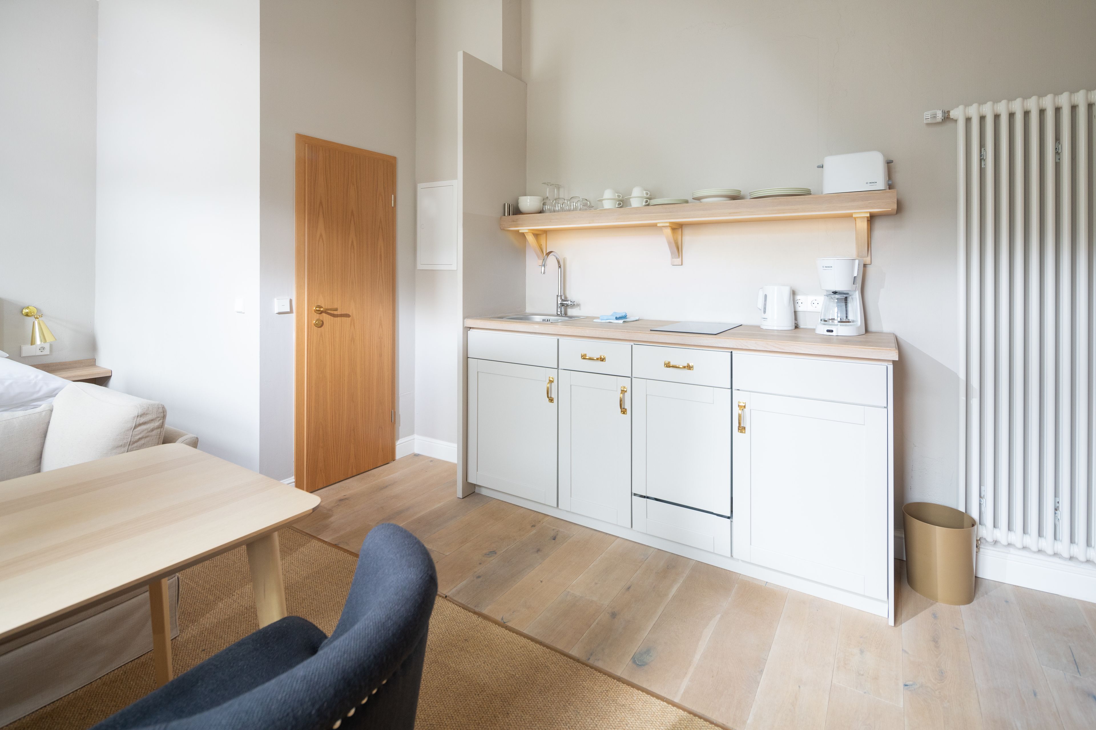 A compact kitchen with white cabinets, a wooden countertop, and a built-in shelf above the sink.
