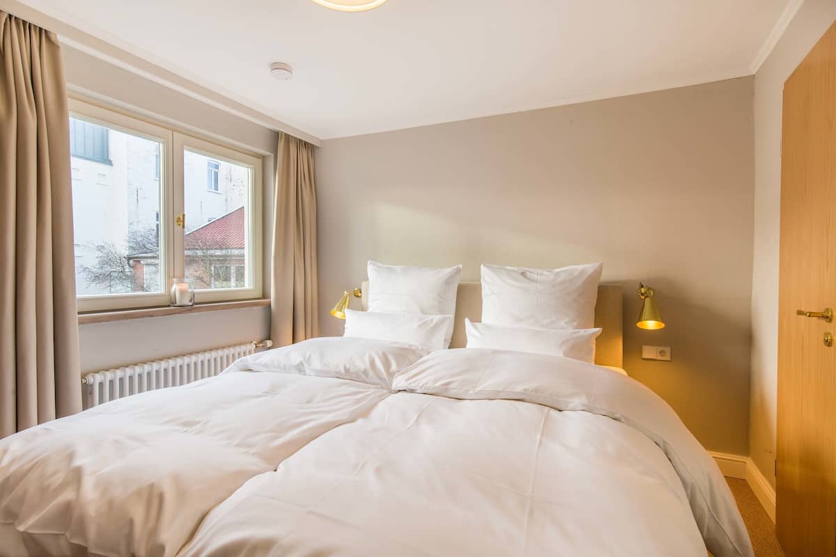A neatly made bed with white linens and two bedside lamps.