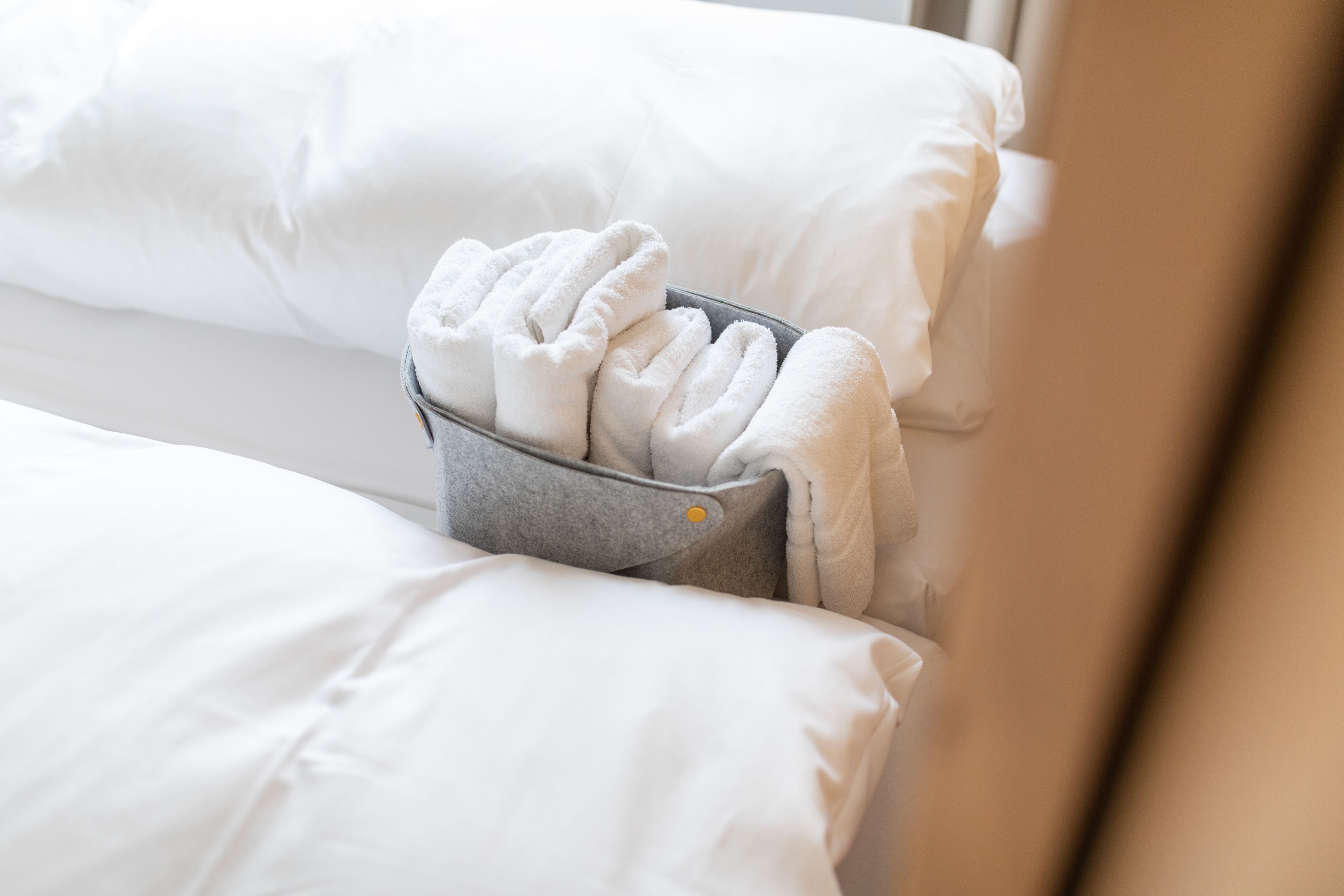 A bed with white linens and a gray towel rack holding several folded towels.