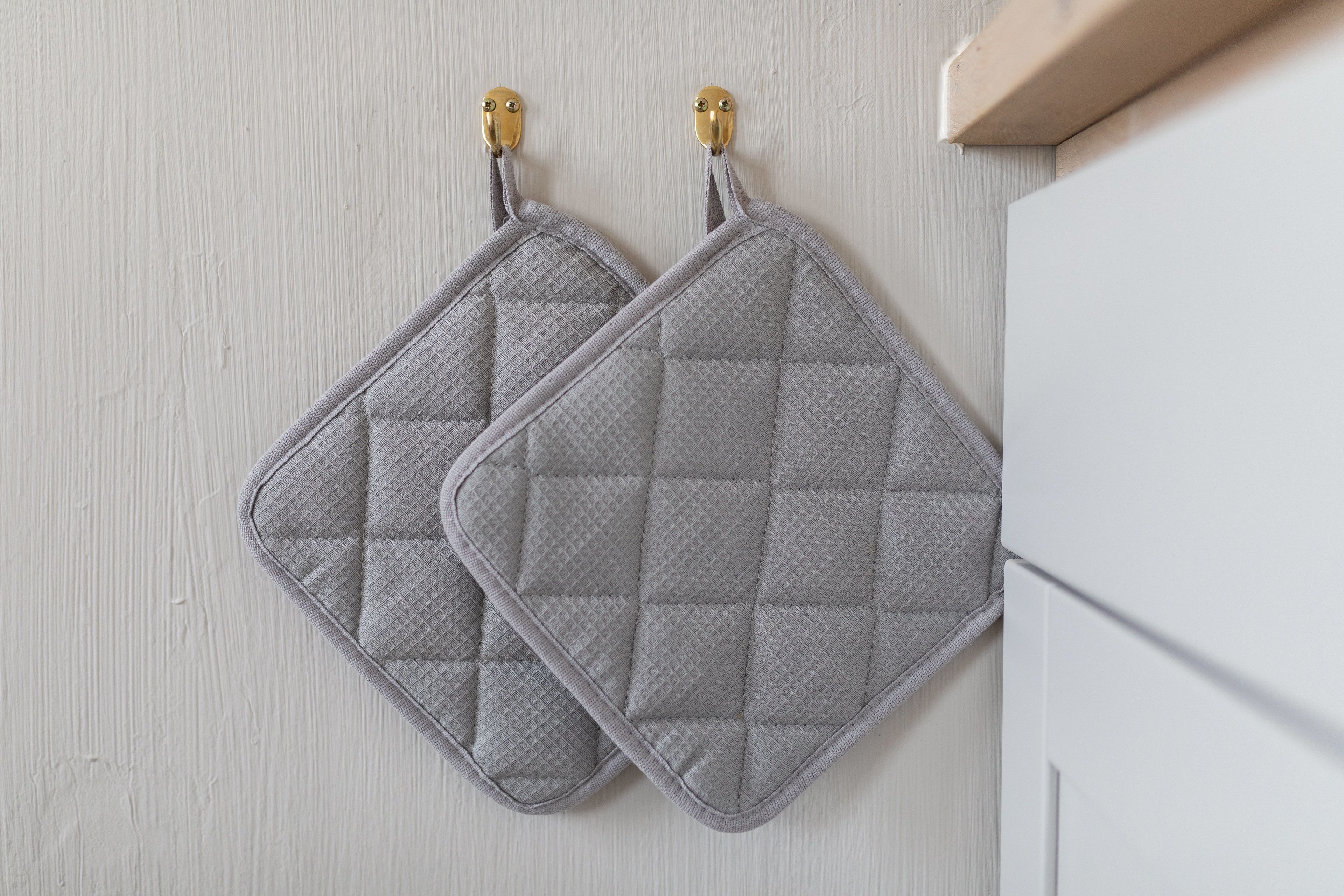 Two gray quilted kitchen mats hanging on a light-colored wooden wall.