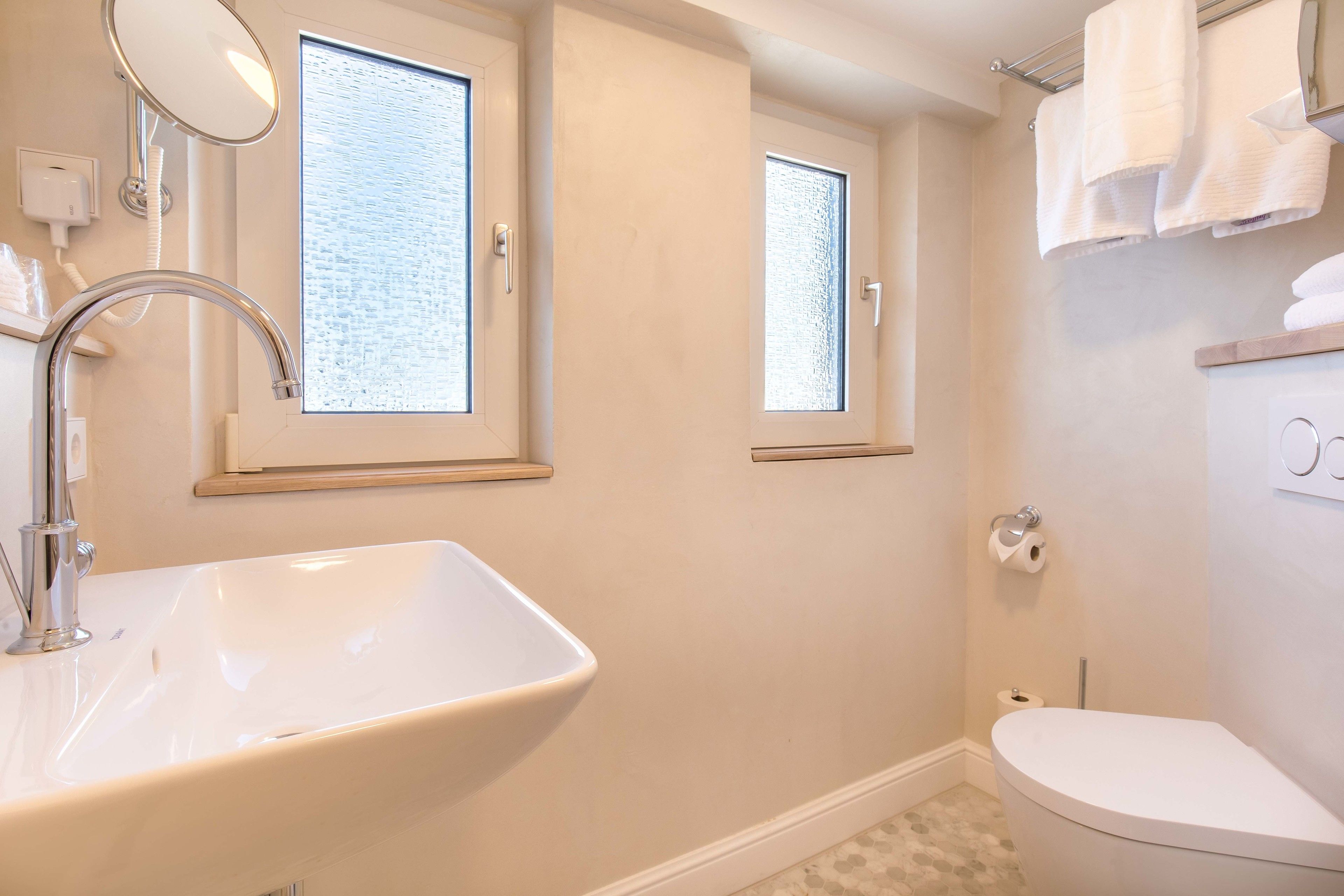 Un baño con un lavamanos grande, un inodoro y dos ventanas.