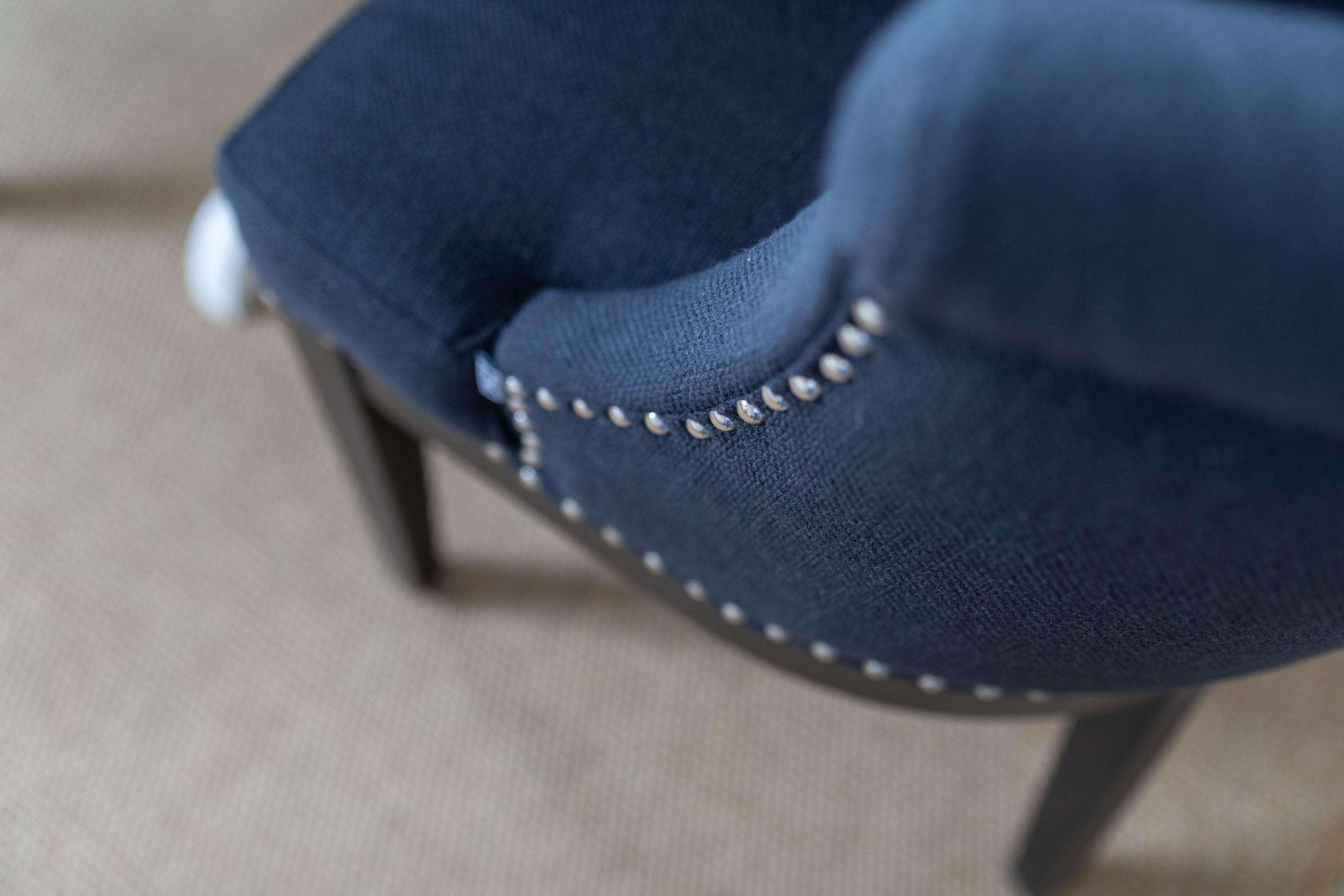 Primer plano del respaldo de una silla con tela oscura y un detalle de cadena metálica decorativa.