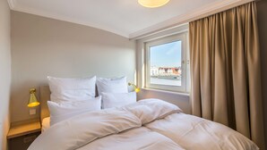 A hotel room with a large bed, two bedside lamps, a window with curtains, and a view of buildings outside.