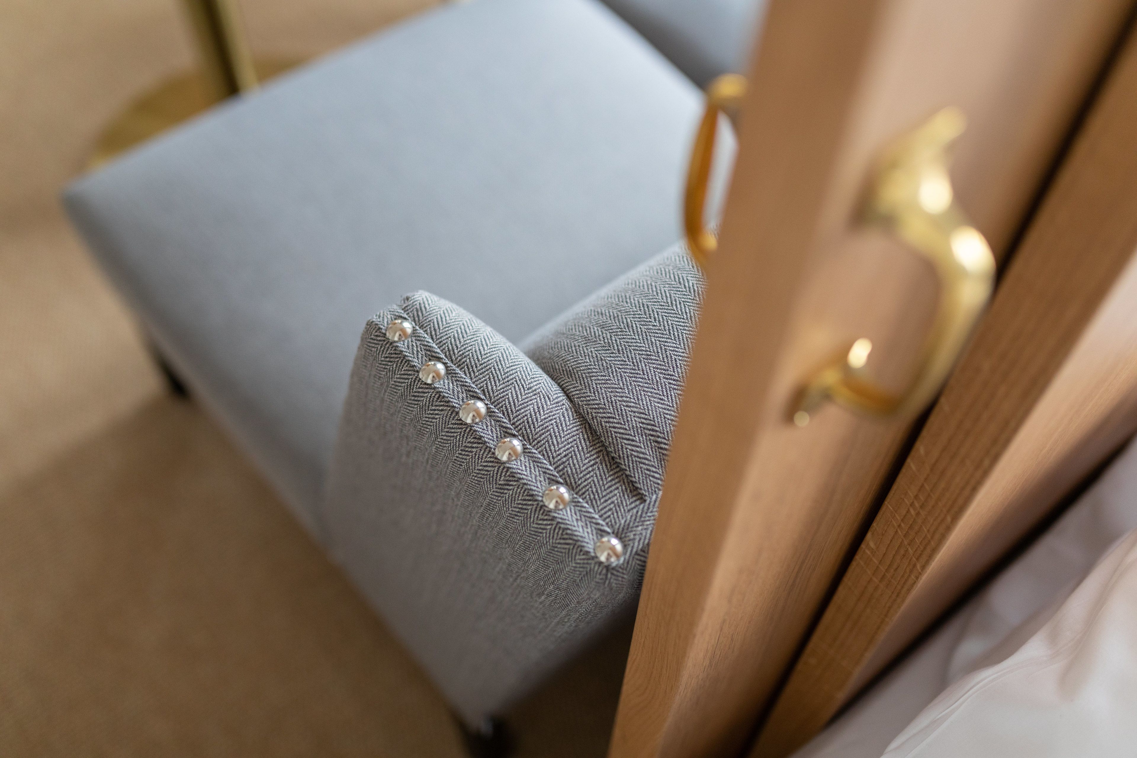 Primer plano de un sillón tapizado en azul claro con estampado de espiga y botones de perla.