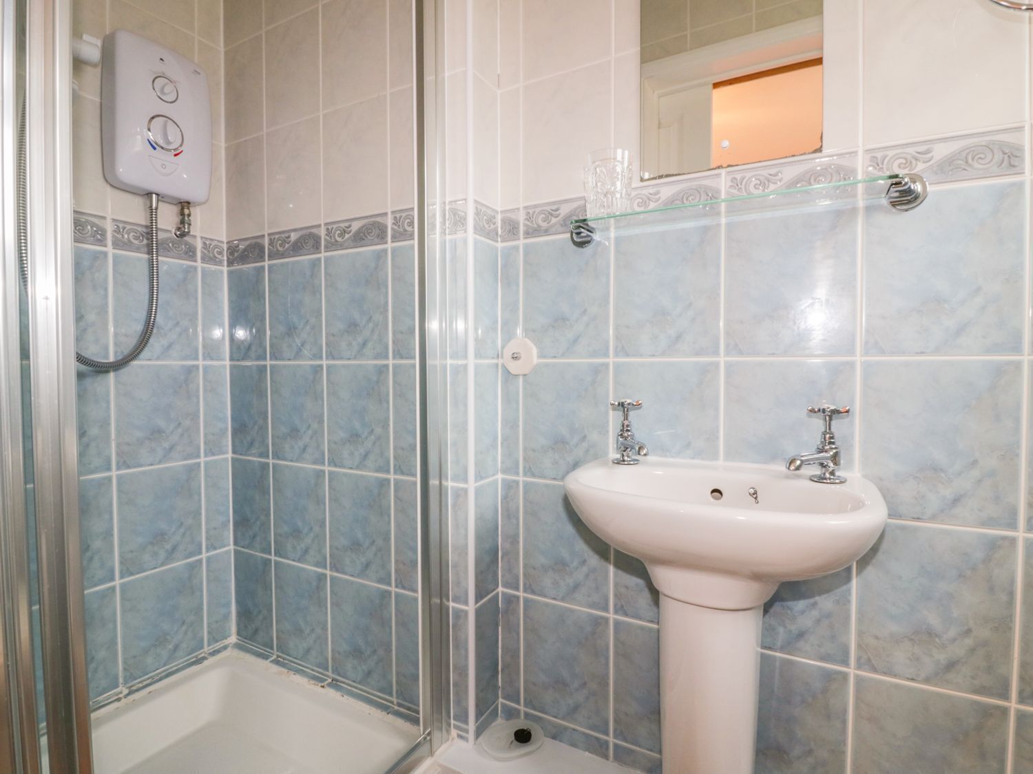Un baño con ducha, lavamanos y mampara de vidrio.