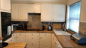 Una cucina moderna con mobili bianchi, forno integrato, microonde, tostapane e lavatrice.