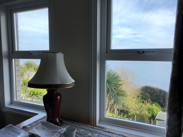 A room with a table, a lamp, and a view of the sea through large windows.