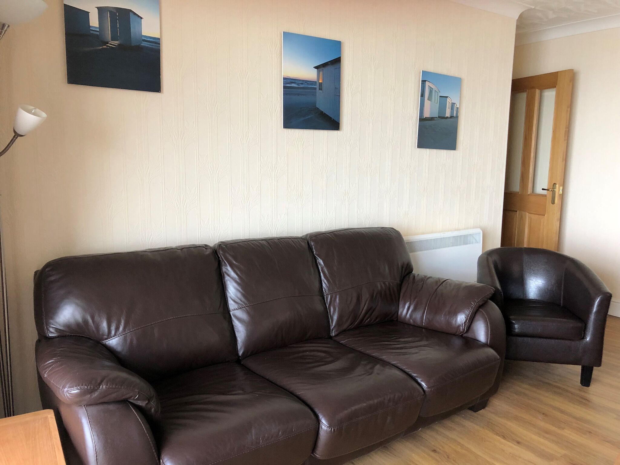Ein braunes Ledersofa in einem Zimmer mit Holzboden, einem weißen Heizkörper und drei gerahmten Bildern an der Wand.