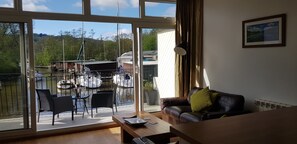 Relax in a spacious living area with a sliding glass door leading to an outdoor space featuring a dining set and a boat docked on the water.
