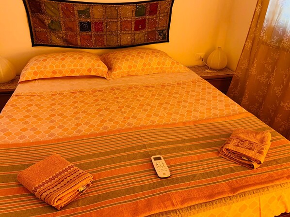 A neatly made bed with a patterned bedspread, two pillows, folded towels, and a remote control on the bed. - a quiet little house in Mondello (Palermo)