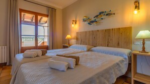 A hotel room with two beds, a wooden headboard, a window with curtains, a wall-mounted light fixture, and a decorative fish wall art piece. - Pretty and calm house, 1km away from the beach (Felanitx)