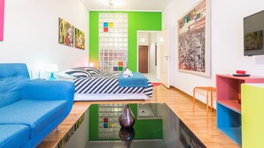 A modern room with a blue sofa, a bed with striped bedding, a green accent wall, and a cityscape painting. - Pop-artment for two in city center (Athina)