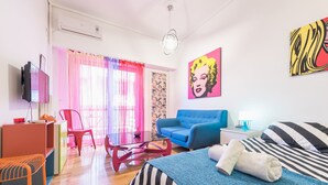 A modern hotel room with a bed, a blue sofa, a TV, and a desk with a chair. - Pop-artment for two in city center (Athina)
