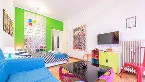 A modern living room with a sofa, a glass coffee table, a television, and a colorful cabinet. - Pop-artment for two in city center (Athina)