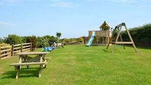A playground with a slide, swings, and picnic tables in a grassy area. - Hazel Cottage Purpose built wheelchair friendly cottage (Truro)