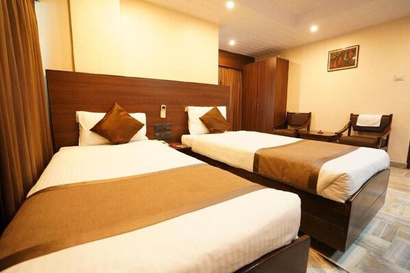Quarto de hotel com duas camas, uma mesa de cabeceira, uma cadeira e um quadro na parede.