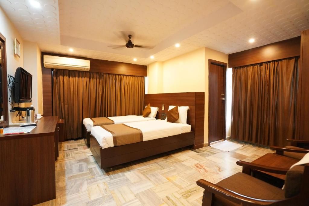 A hotel room with a large bed, a desk, a chair, an air conditioning unit, and a television.
