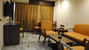 A hotel room with a sofa, chairs, a small table, a TV, and an air conditioning unit. - Jaya Residency (Kakinada)