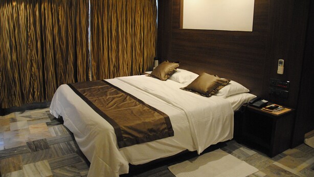 A hotel room with a large bed, a bedside table with a phone and a lamp, and a curtain-covered window. - Jaya Residency (Kakinada)