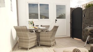 Une terrasse dotée de meubles en osier, d’une table mise avec des verres à vin et une bouteille, et d’un barbecue.