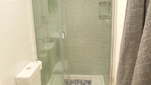 Une douche fermée par des parois en verre, avec un sol carrelé, des toilettes et un porte-serviettes.