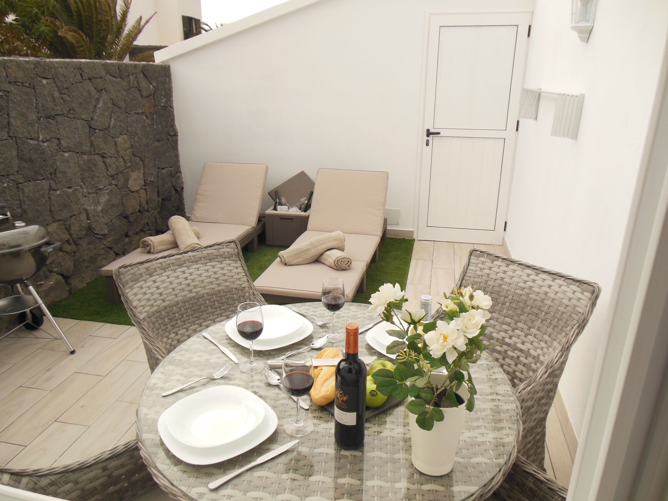 A patio with a round table set for dining, a grill, and a seating area with cushions and a sofa.