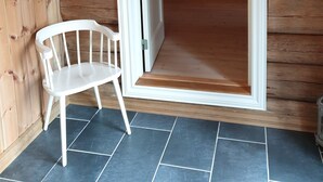 A wooden cabin interior with a white door leading to a room, a white chair, and a heart-shaped decoration on the wall.