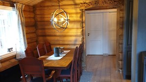 A wooden cabin interior with a dining table, chairs, a chandelier, and a fireplace.