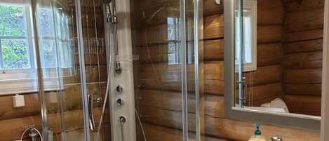 A modern bathroom with a glass-enclosed shower, a sink with a wooden countertop, and a large mirror.