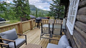 A wooden deck with outdoor furniture, including chairs and a sofa, overlooking a scenic landscape with trees and a mountain in the background.