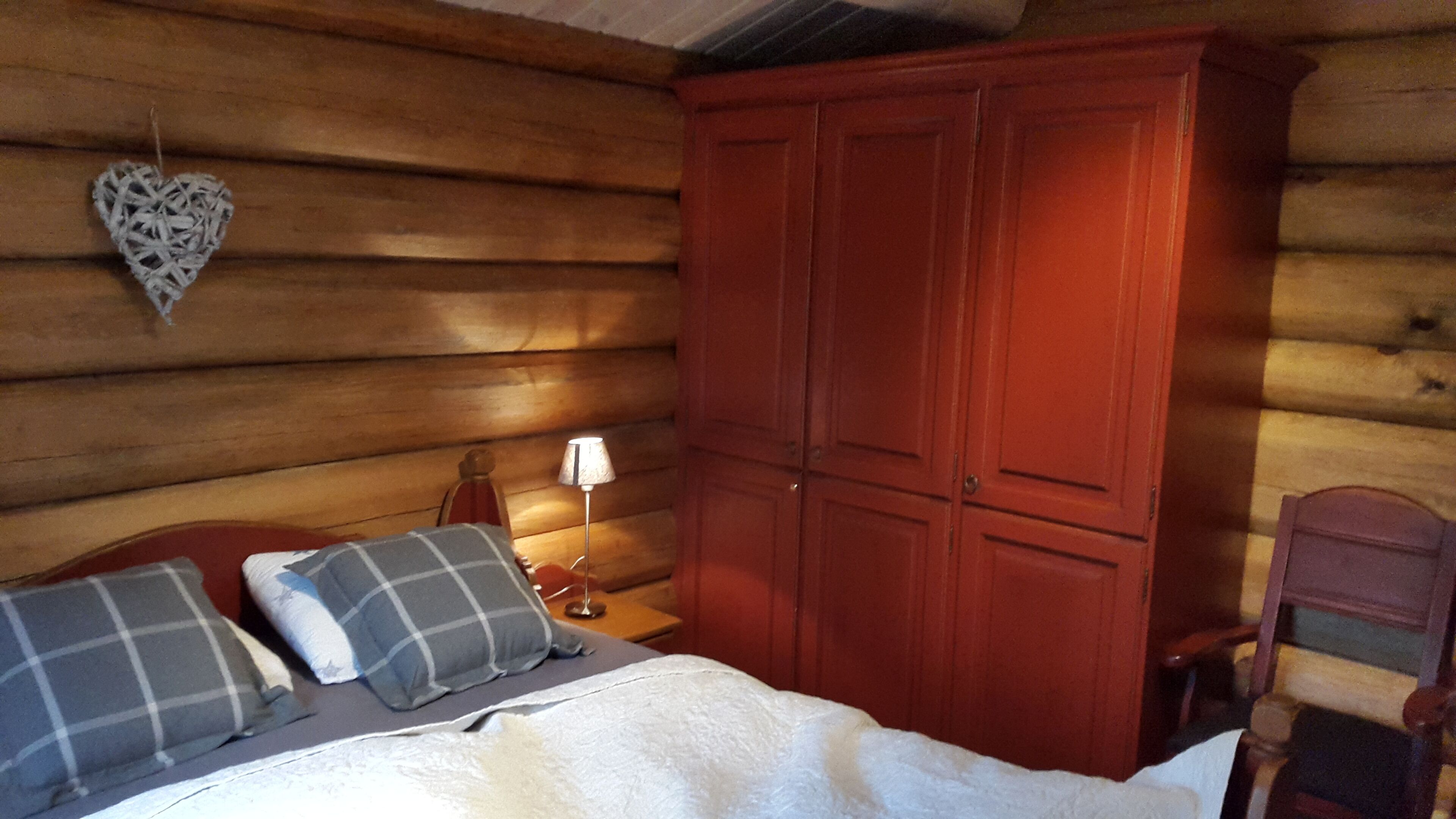 Una habitación de cabaña de madera con una cama, dos almohadas, una mesita de noche, una lámpara y un armario.