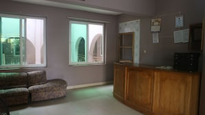 A room with two large windows, a wooden cabinet, and a patterned sofa.