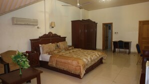 A bedroom with a large bed, a wooden wardrobe, a desk with a chair, and a ceiling fan.