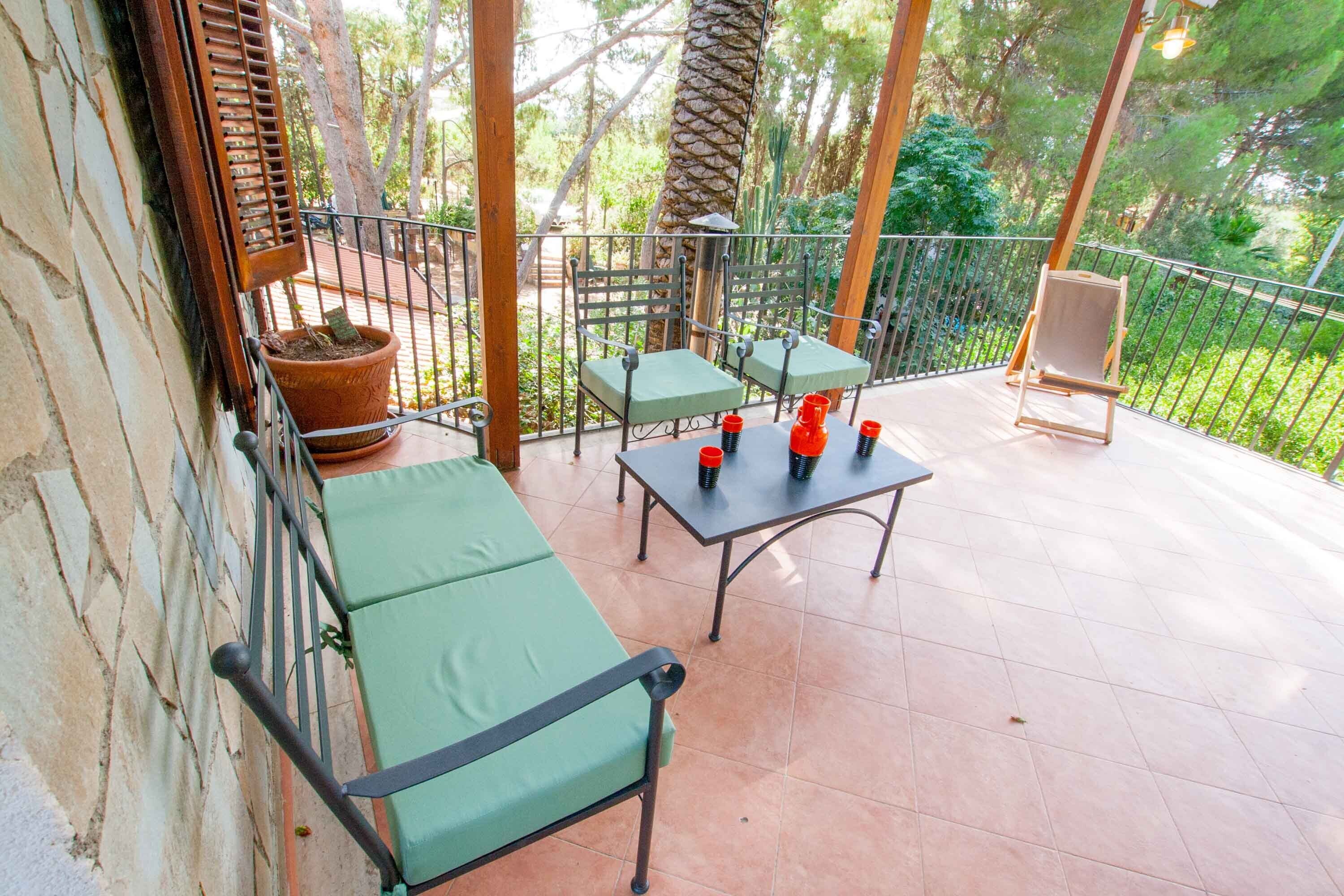 A terrace with green cushioned seating, a table with red cups, and a potted plant.