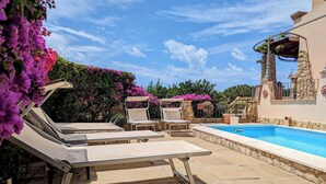 Zona junto a la piscina con sillones de descanso, una piscina y un muro de piedra con plantas.