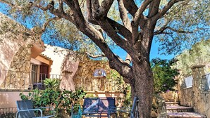 Un patio con suelo de piedra, un gran árbol y mobiliario exterior.