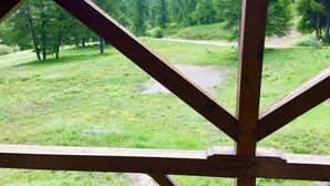 Une vue à travers une structure en bois, avec un champ herbeux et une colline boisée en arrière-plan.