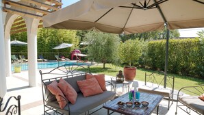 Patio esterno con divano, tavolo con ciotole e piscina sullo sfondo.