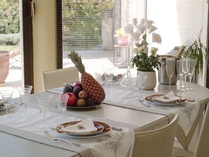 A dining table set for a meal with a fruit bowl, wine glasses, and a vase of flowers.