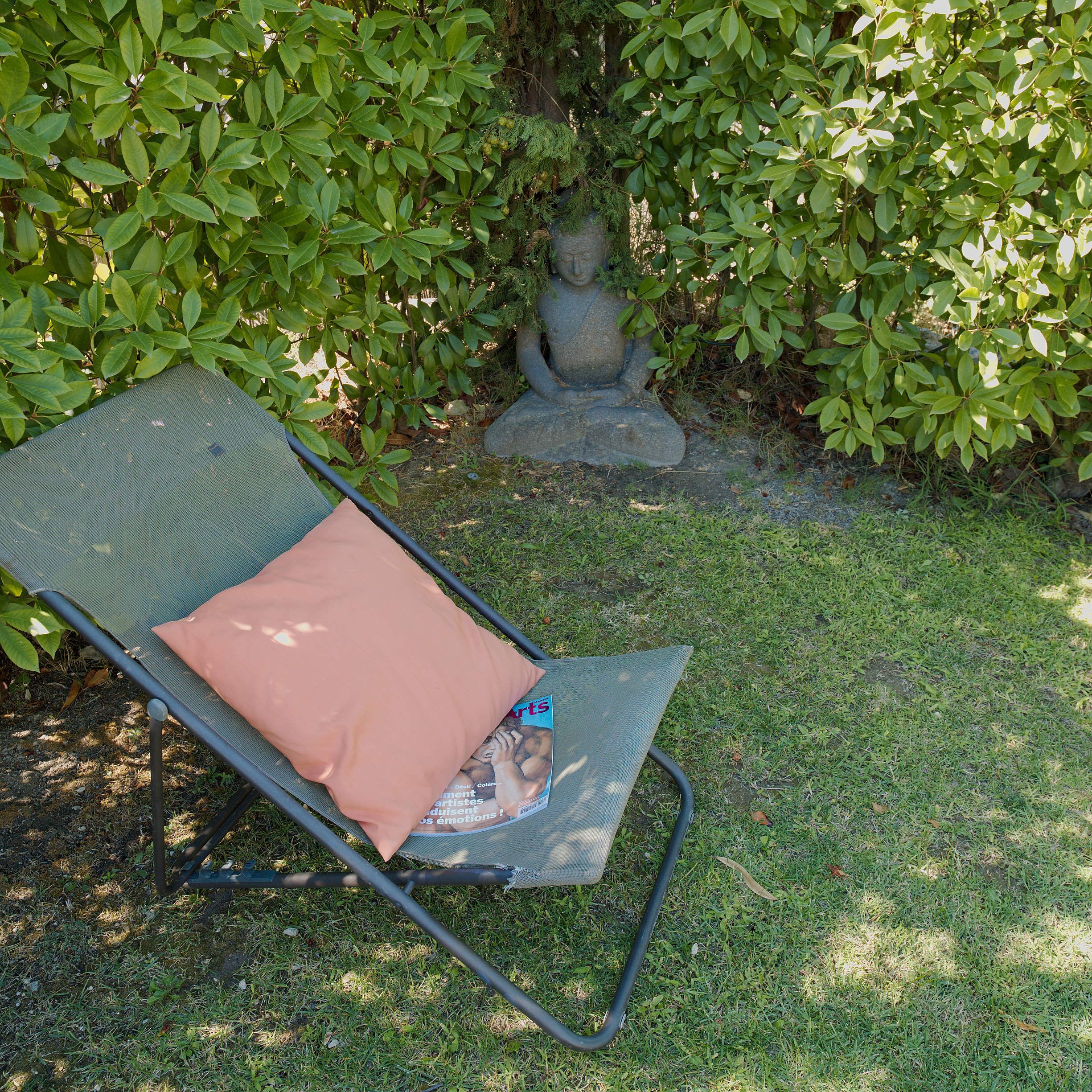 A garden with a metal chair and a statue.