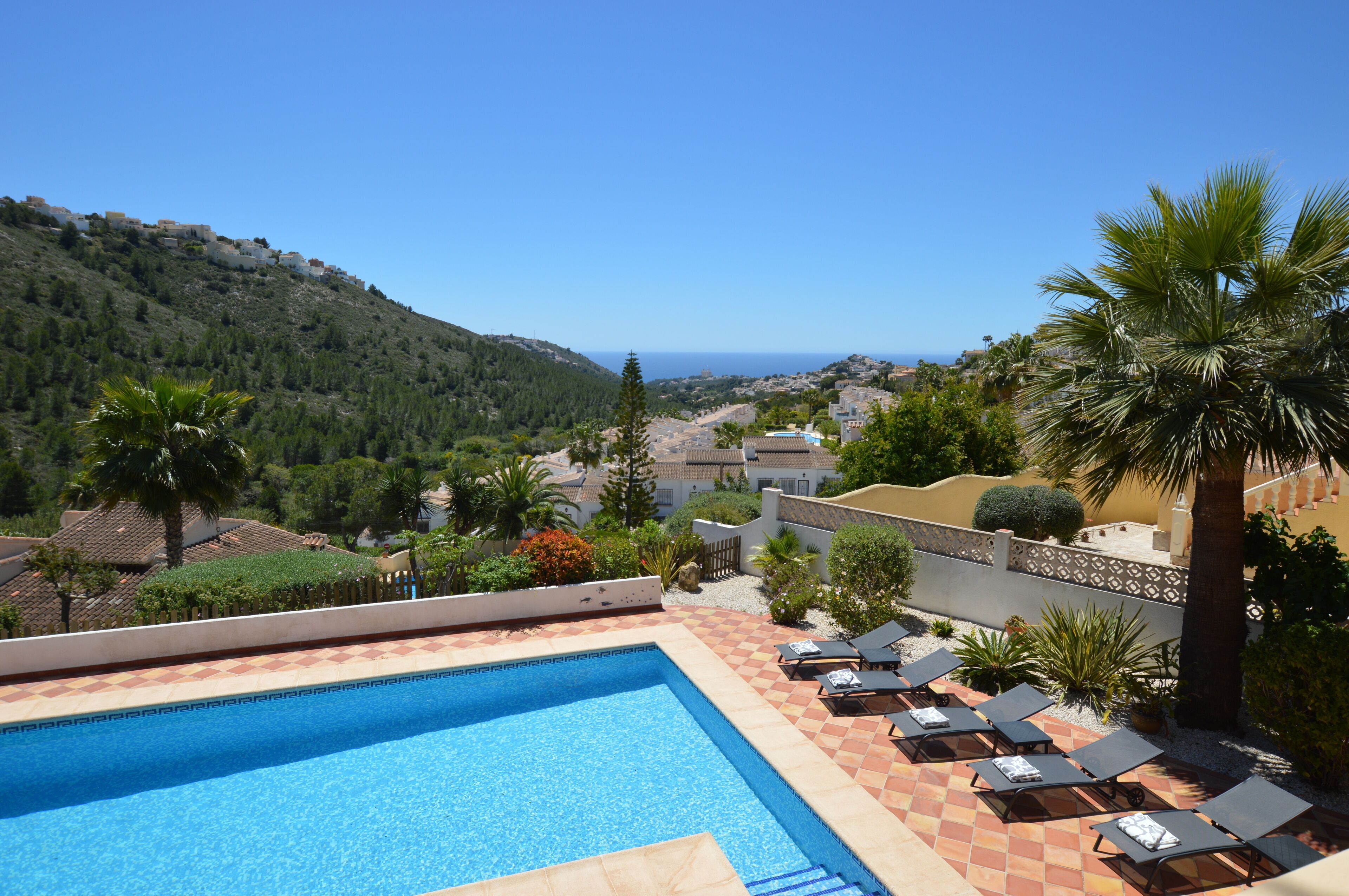A swimming pool with lounge chairs and a view of the sea and hills.