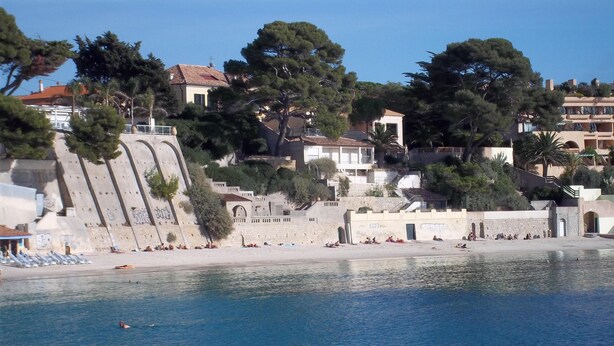 Una zona costera con playa de arena, costa rocosa y edificios con balcones que dan al mar.
