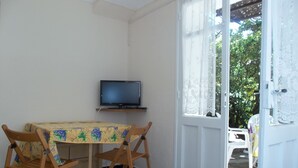 Una habitación pequeña con una televisión en un estante, una mesa con mantel floreado y dos sillas de madera.