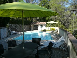 A swimming pool with a stone wall, lounge chairs, and a table with chairs.