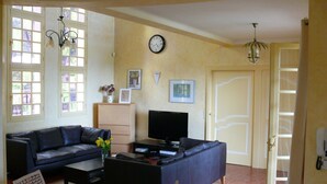 A living room with a sofa, coffee table, TV, and a clock on the wall. - Beautiful House With Tower Close To The Picturesque Town Of Lorgues. (Lorgues)