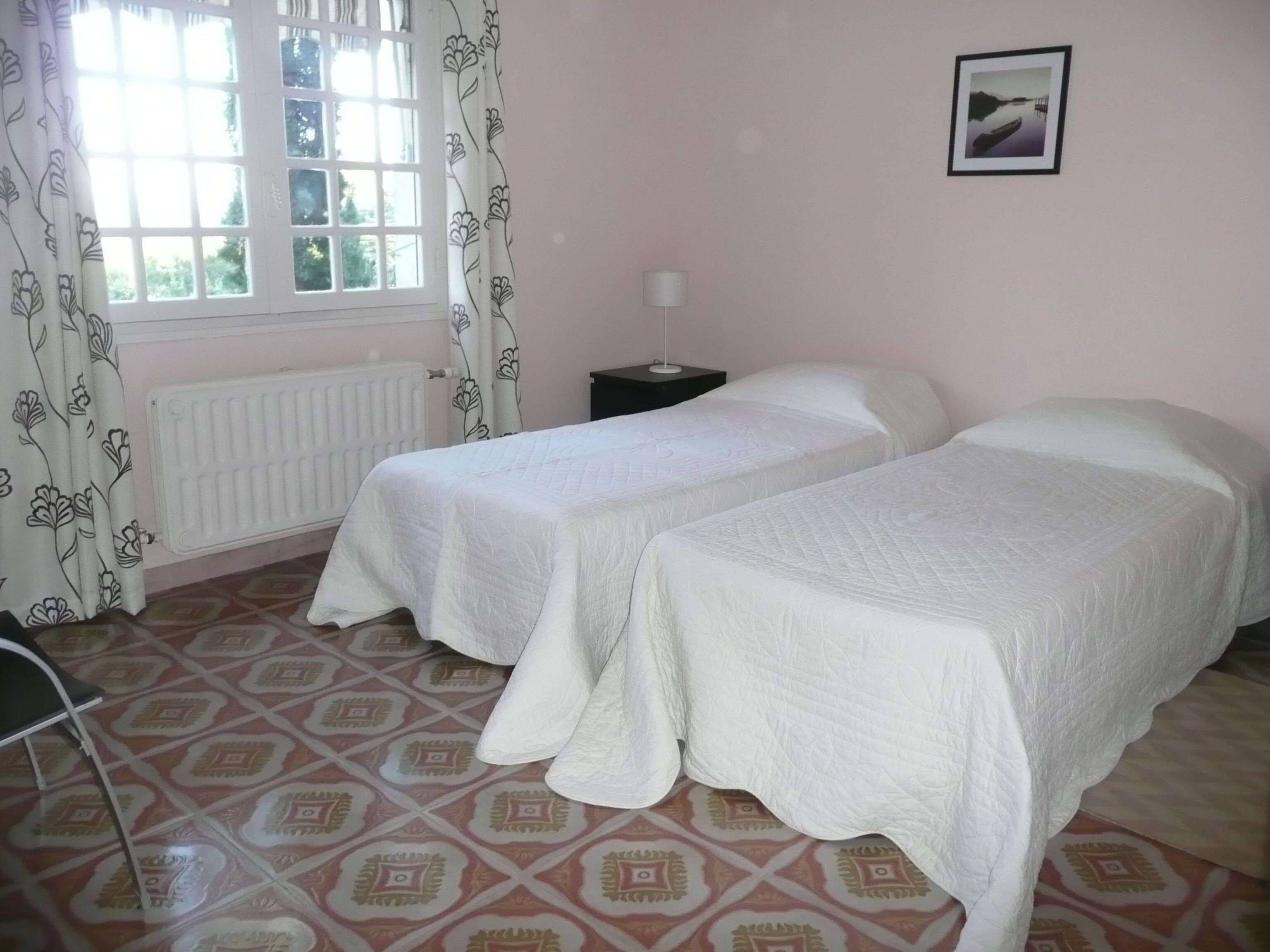 A room with two beds, a radiator, a nightstand, and a window with curtains.