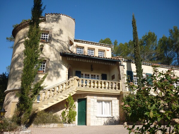 A historic building with a stone staircase leading to a balcony, a green door, and a tiled roof.