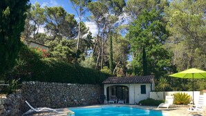 A swimming pool with lounge chairs and a covered seating area, surrounded by trees and a stone wall. - Beautiful House With Tower Close To The Picturesque Town Of Lorgues. (Lorgues)